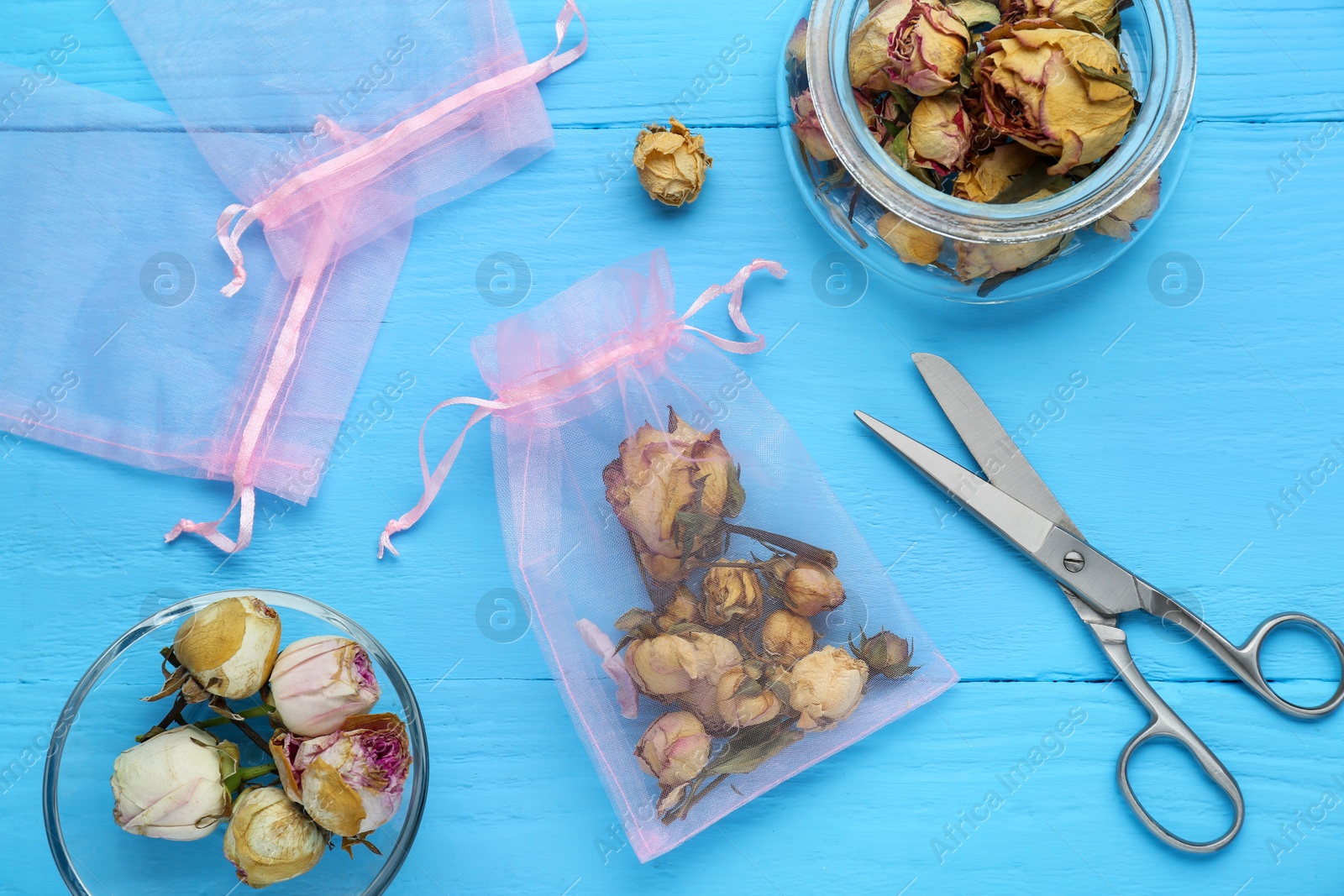 Photo of Scented sachet with dried roses and scissors on light blue wooden table, flat lay