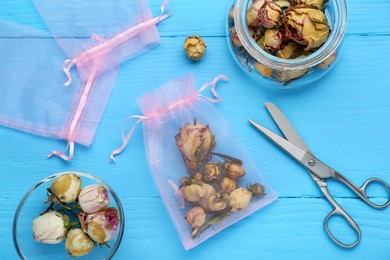 Scented sachet with dried roses and scissors on light blue wooden table, flat lay