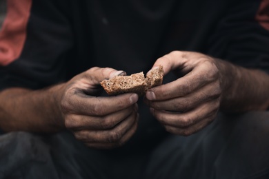 Poor homeless with piece of bread outdoors, closeup