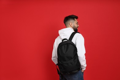 Photo of Young man with stylish backpack on red background, back view. Space for text