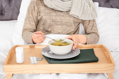 Photo of Sick young woman eating broth to cure cold in bed at home