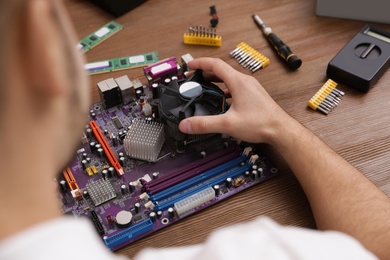 Photo of Male technician repairing motherboard at table, closeup