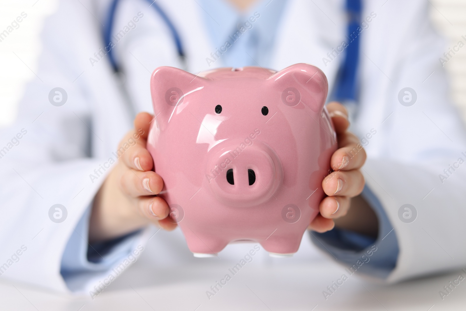 Photo of Doctor with piggy bank at white table, closeup