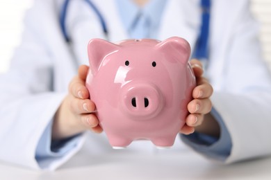 Photo of Doctor with piggy bank at white table, closeup