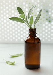 Bottle of sage essential oil and fresh herb on white table