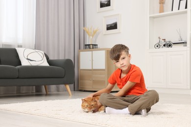 Photo of Little boy petting cute ginger cat on soft carpet at home, space for text