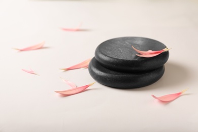 Photo of Stacked spa stones with flower petals on light background. Space for text