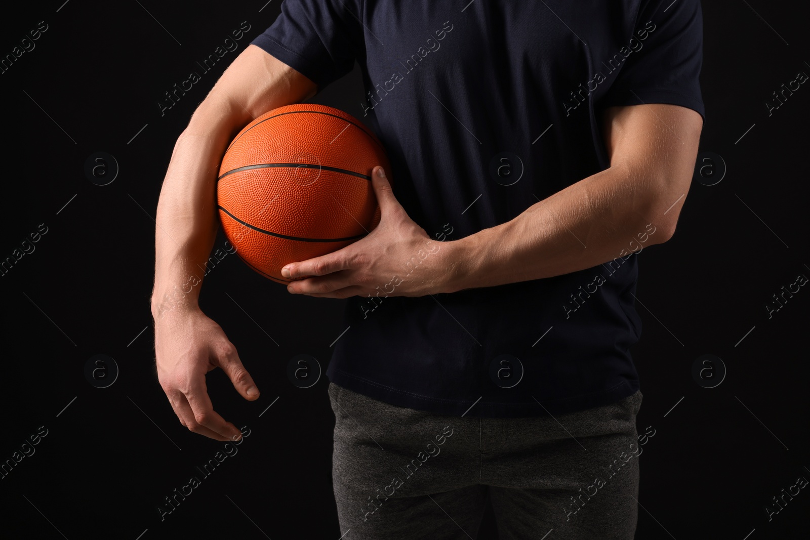 Photo of Athletic man with basketball ball on black background, closeup