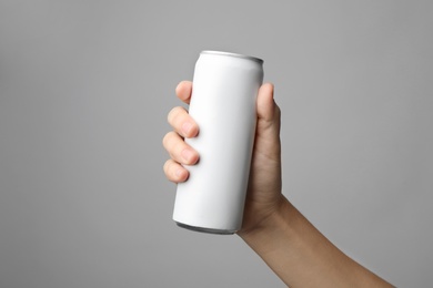 Woman holding aluminum can with beverage on grey background, closeup. Space for design