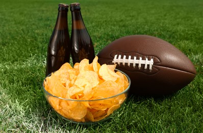 Photo of American football ball with beer and chips on green field grass outdoors