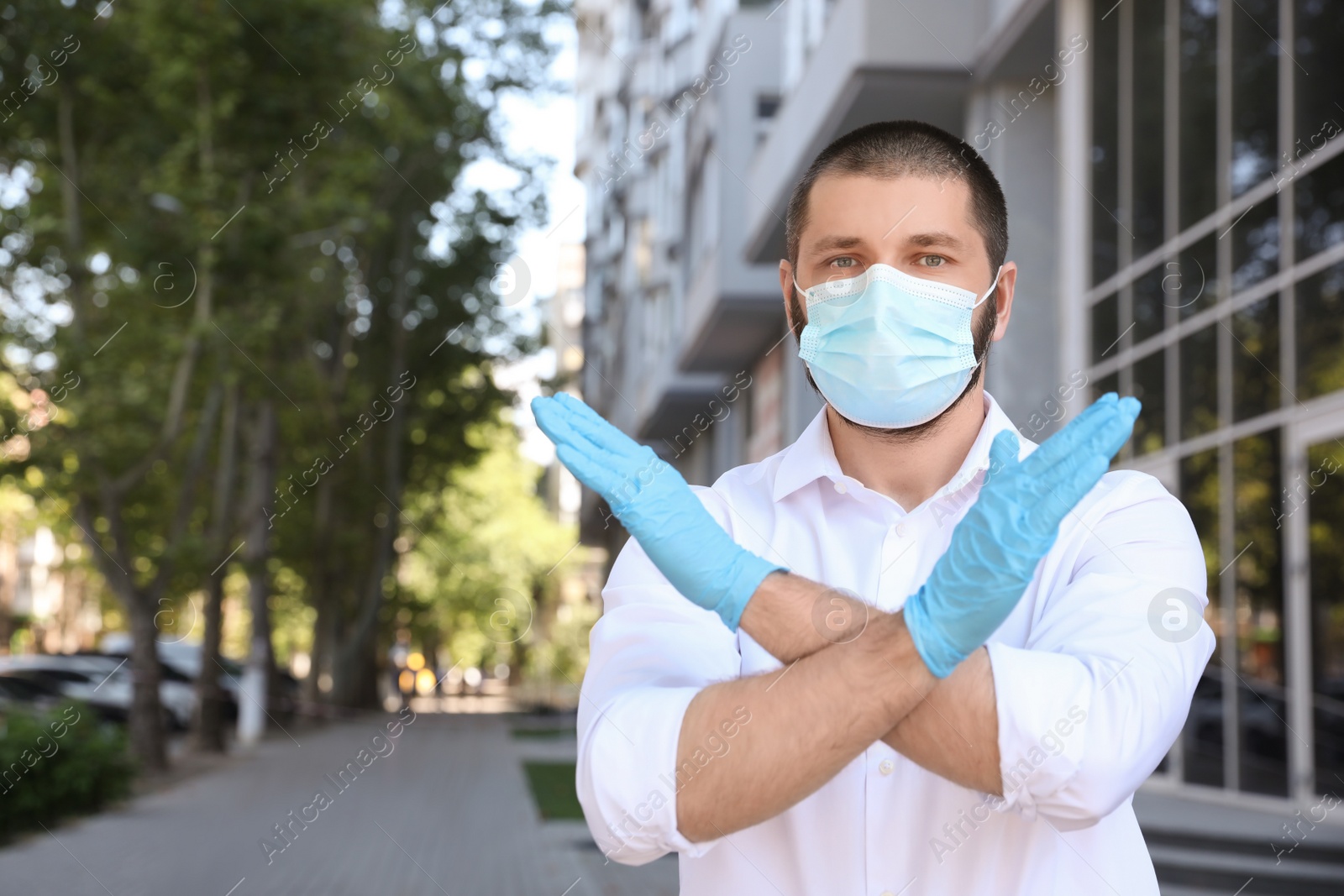 Photo of Man in protective face mask showing stop gesture outdoors. Prevent spreading of coronavirus