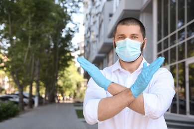 Man in protective face mask showing stop gesture outdoors. Prevent spreading of coronavirus