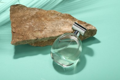 Bottle of luxury perfume in sunlight and stone on turquoise background, above view