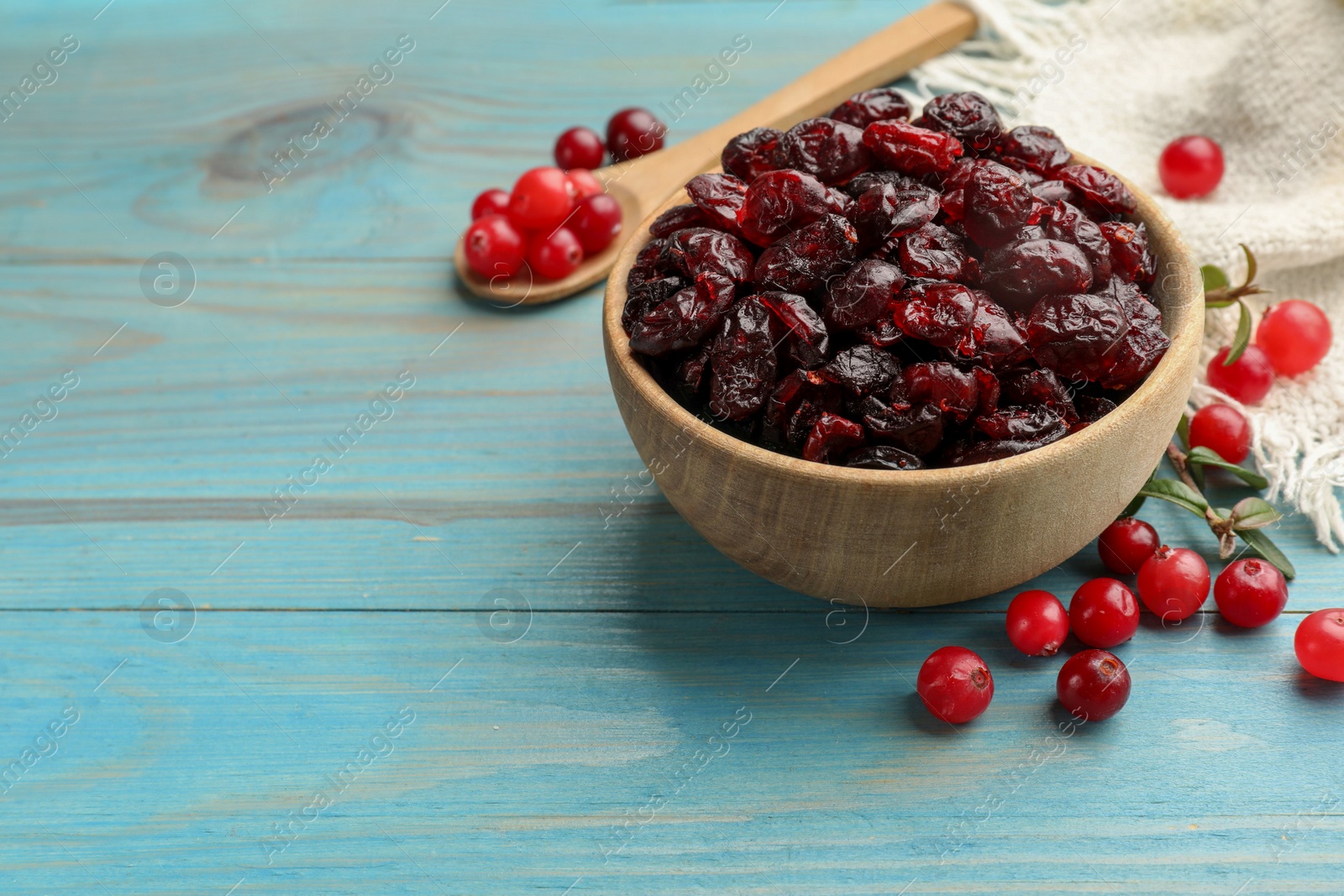 Photo of Tasty dried cranberries in bowl and fresh ones on light blue wooden table. Space for text