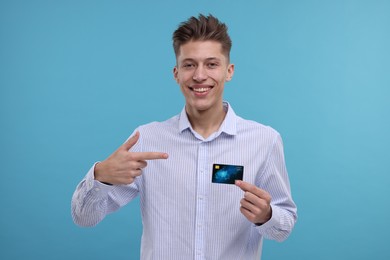 Photo of Happy man pointing at credit card on light blue background