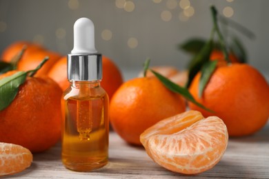 Bottle of tangerine essential oil and fresh fruits on white wooden table, closeup