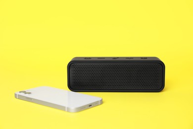 Portable bluetooth speaker and smartphone on yellow background. Audio equipment