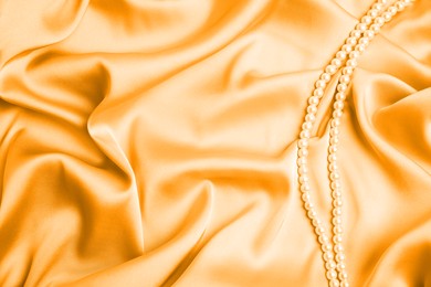 Image of Beautiful pearls on light orange silk, top view