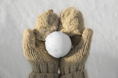 Photo of Woman in knitted mittens holding snowball outdoors, top view