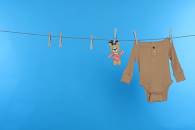 Baby onesie and bear toy drying on laundry line against light blue background, space for text