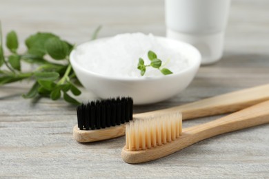 Photo of Toothbrushes, salt and green herbs on wooden table, closeup