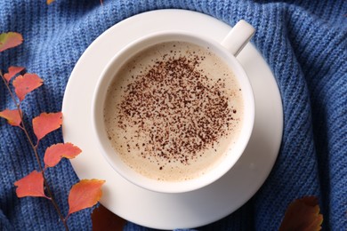 Cup of hot drink and leaves on blue knitted fabric, flat lay. Cozy autumn atmosphere