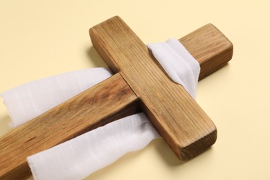 Photo of Wooden cross and white cloth on beige background, closeup. Easter attributes