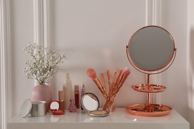 Photo of Mirror and makeup products on white dressing table near wall