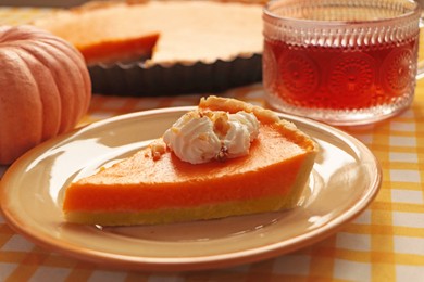 Photo of Piece of fresh homemade pumpkin pie served with whipped cream and tea on table, closeup