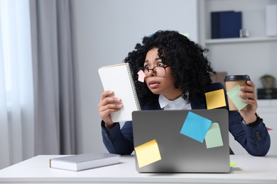 Photo of Deadline concept. Stressed woman looking at notepad and holding paper cup in office, space for text. Sticky notes everywhere as reminders