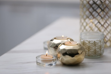 Photo of Burning candles in holders on white marble table indoors