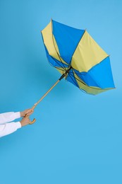 Woman with umbrella caught in gust of wind on light blue background, closeup