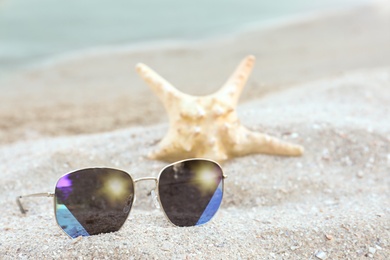 Stylish sunglasses and starfish on sandy beach