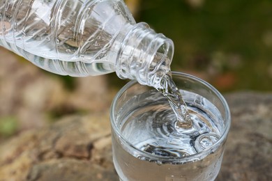 Photo of Pouring water from bottle into glass outdoors, closeup