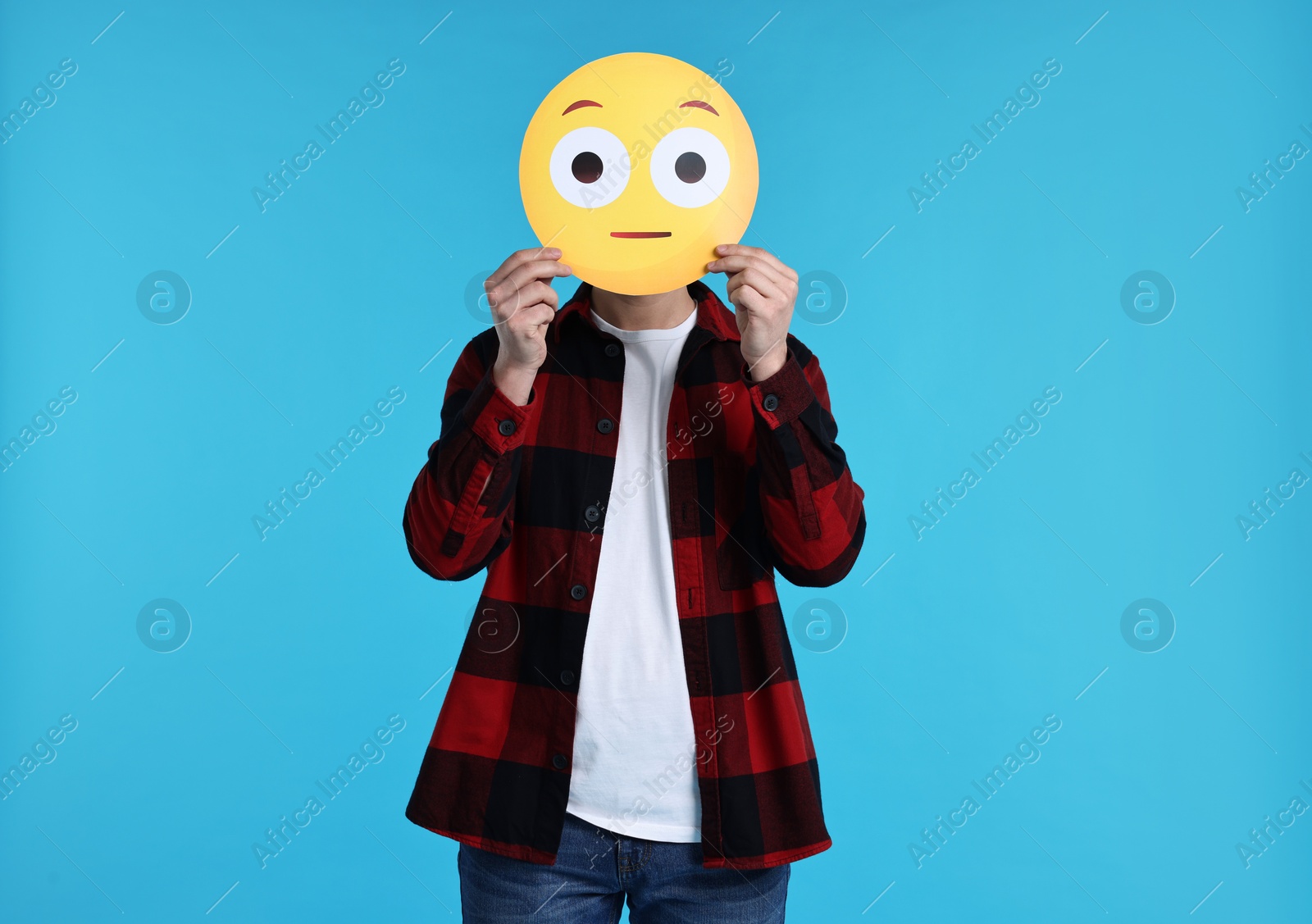 Photo of Man covering face with surprised emoticon on light blue background