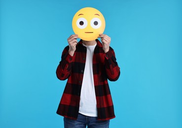 Photo of Man covering face with surprised emoticon on light blue background