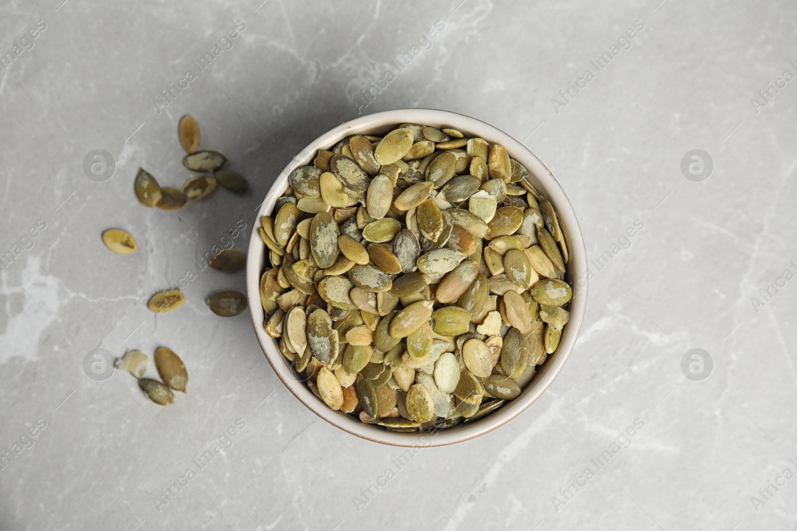 Photo of Bowl of raw pumpkin seeds on light grey marble table, top view