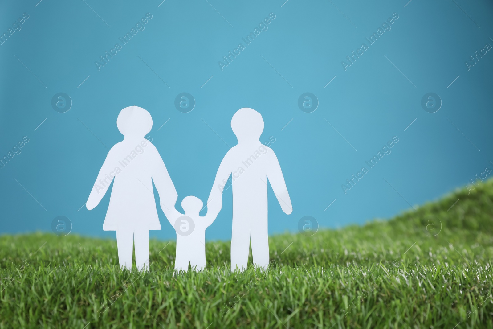 Photo of Paper cutout of parents with their child on green grass against light blue background, space for text. Family Day