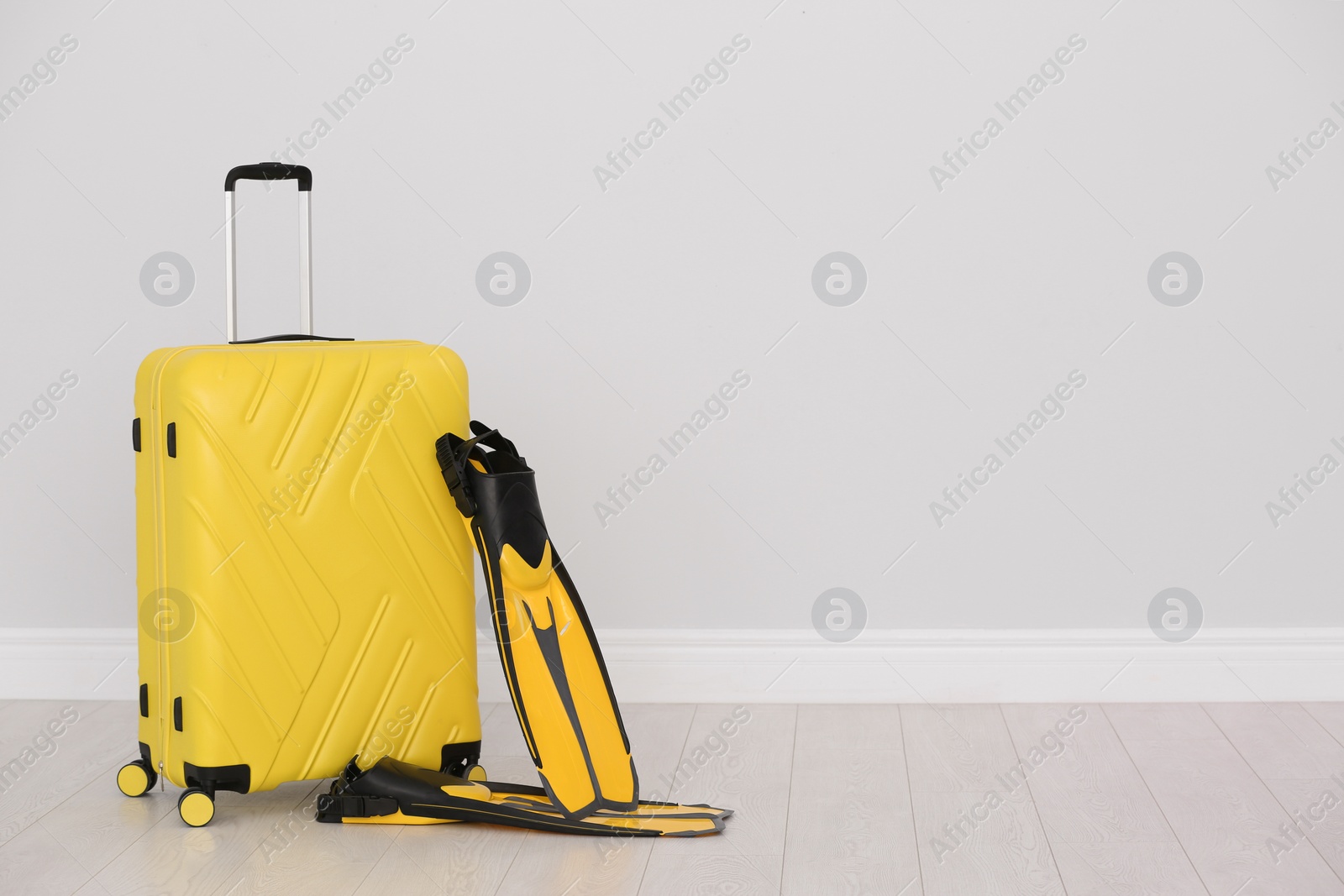 Photo of Modern suitcase and flippers on floor near light wall. Space for text
