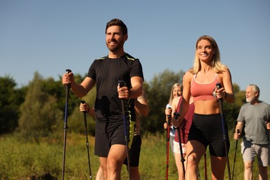 Photo of Group of happy people practicing Nordic walking with poles outdoors on sunny day