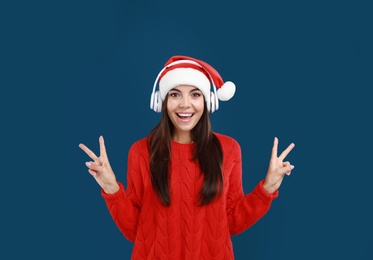 Young woman in Santa hat listening to Christmas music on dark blue background