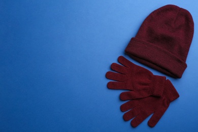 Photo of Woolen gloves and hat on blue background, flat lay. Space for text