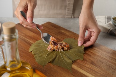 Photo of Woman preparing stuffed grape leaves on wooden board, closeup