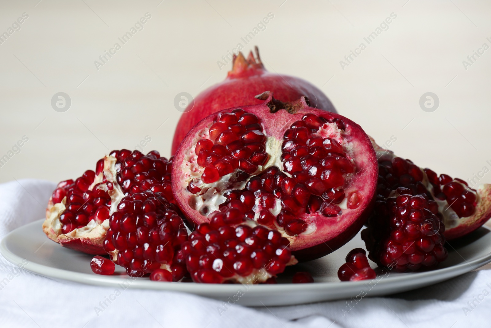 Photo of Plate with ripe pomegranates on table against light background