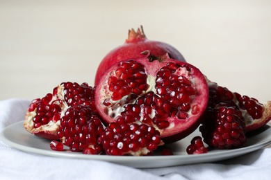 Photo of Plate with ripe pomegranates on table against light background