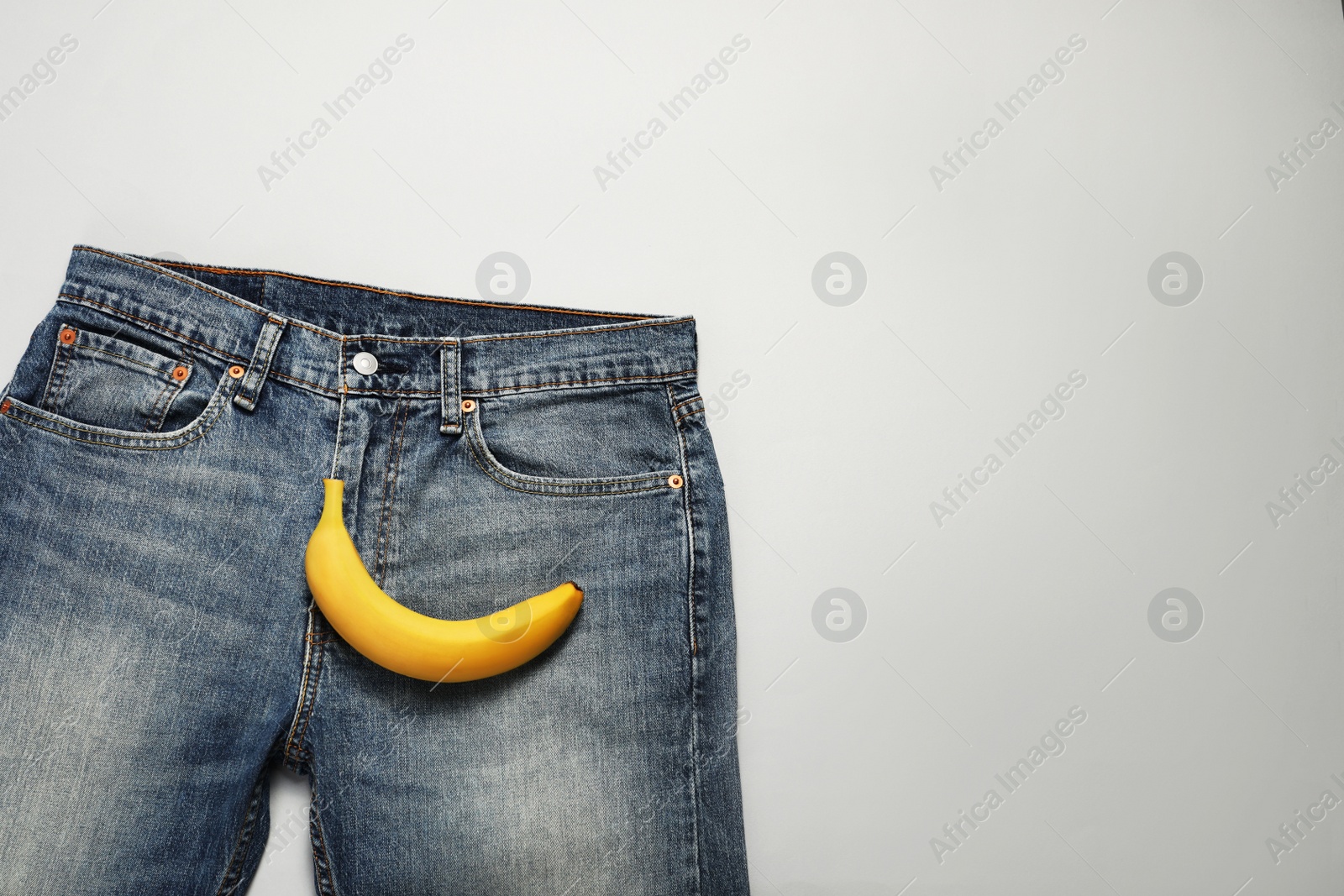 Photo of Men jeans with banana on light grey background, top view and space for text. Potency concept