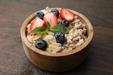 Photo of Tasty oatmeal with strawberries, blueberries and almond petals in bowl on wooden table, closeup