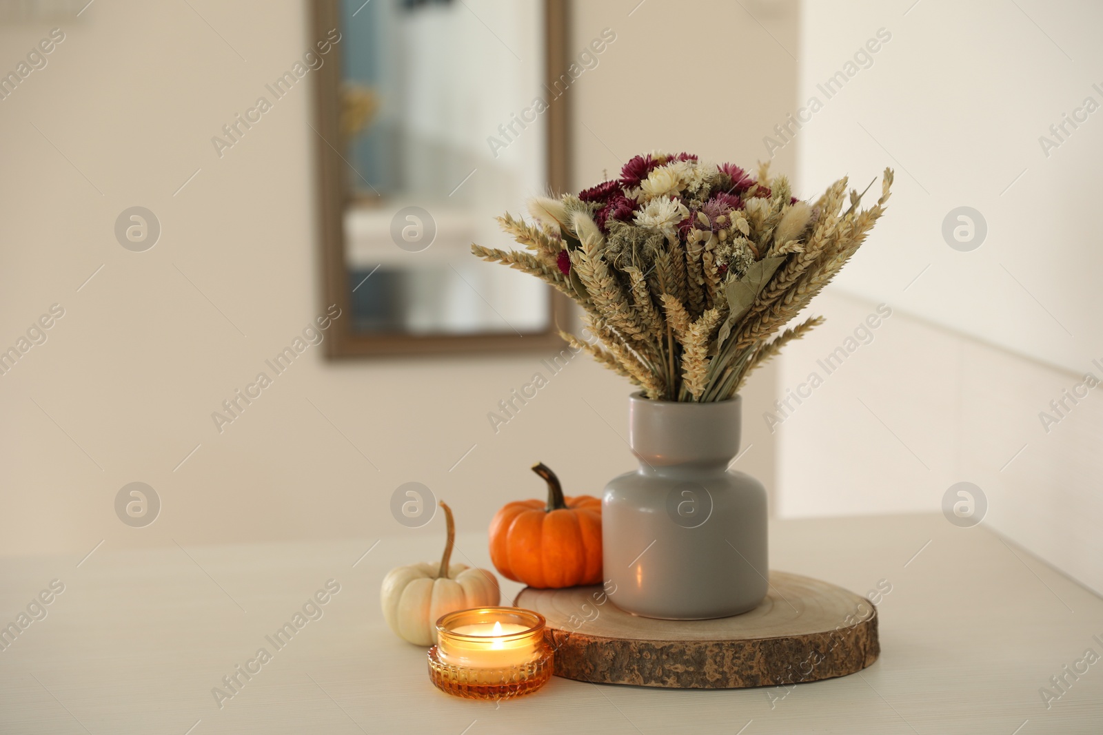 Photo of Beautiful bouquet of dry flowers, small pumpkins and candle on white table indoors, space for text