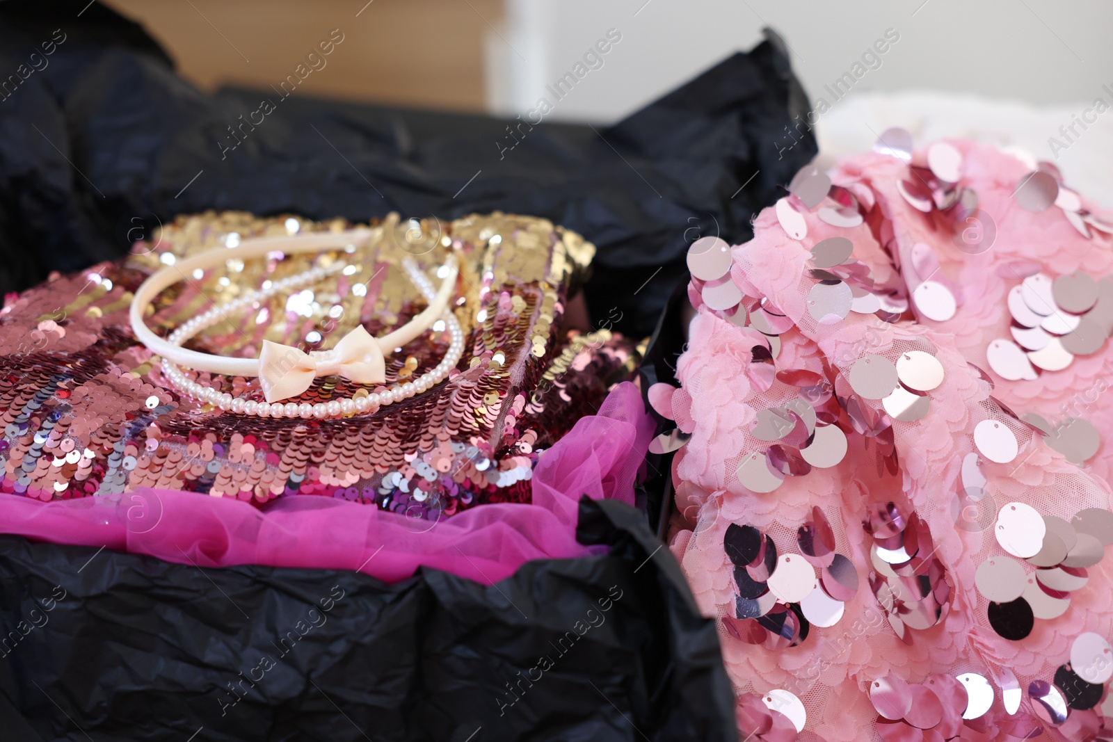 Photo of Headbands and stylish pink carnival costume with sequins in black box, closeup