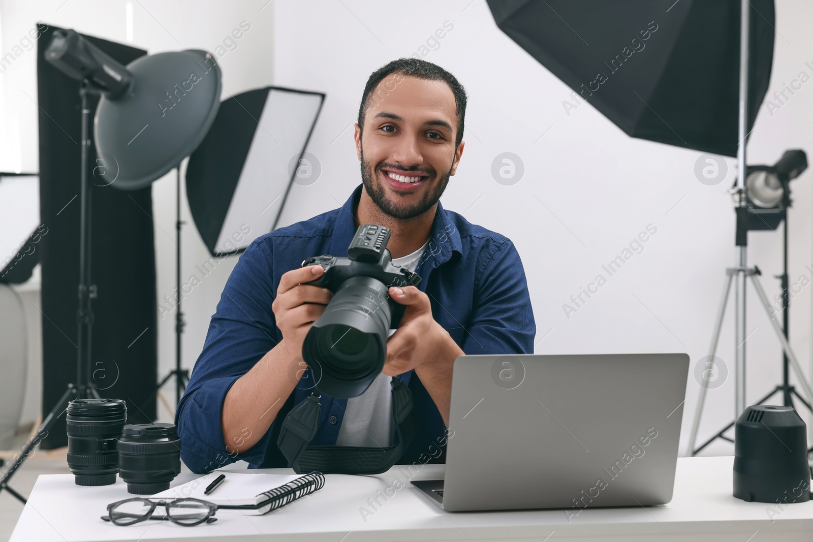 Photo of Young professional photographer with camera at table in modern photo studio